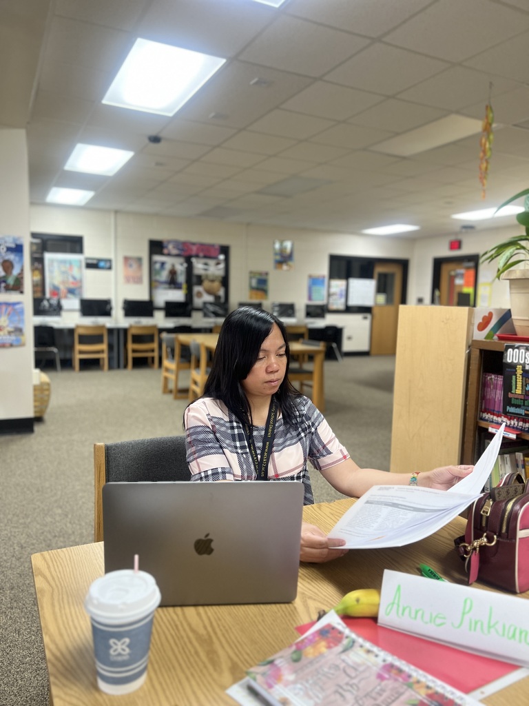 Female teacher sitting down and reading a worksheet.